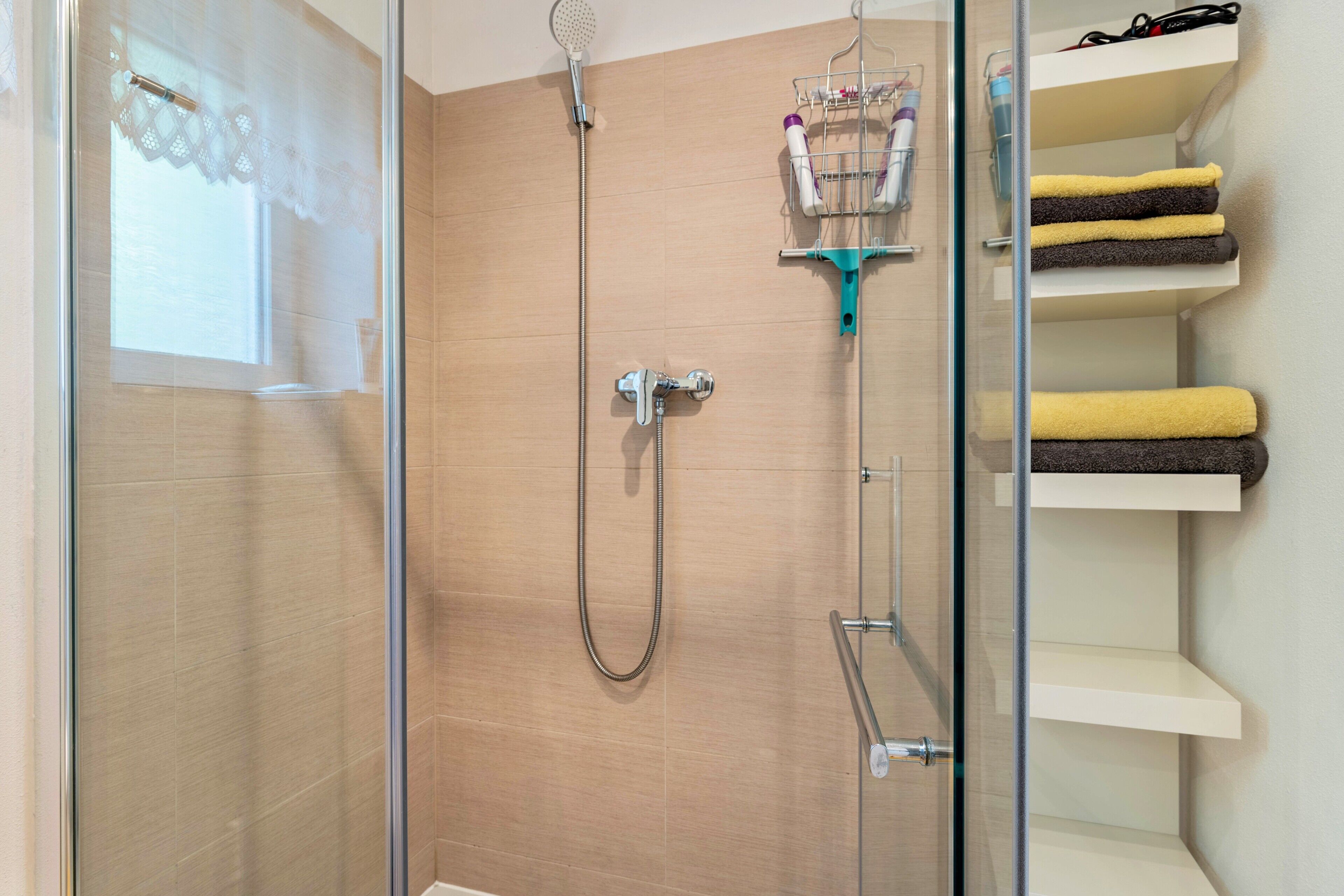 Eine Dusche mit Glastür, ein Handtuchhalter mit Handtüchern und ein Ablagefach mit Pflegeprodukten.