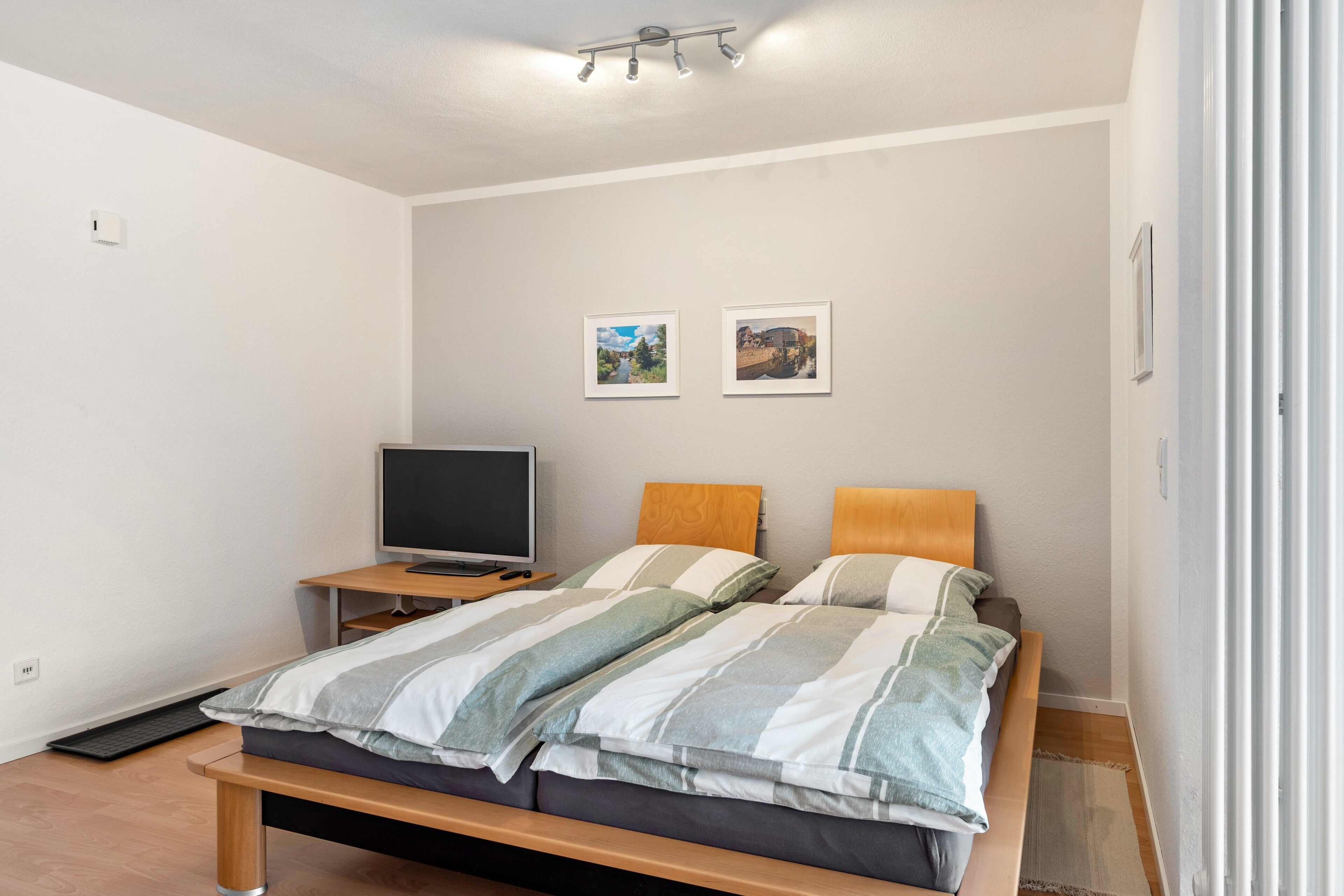 Quarto com cama, televisão e duas quadros pendurados na parede.