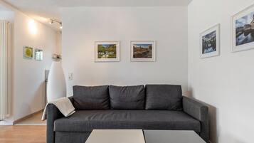 Een moderne woonkamer met een grijze bank, een witte salontafel en drie ingelijste foto’s aan de muur.