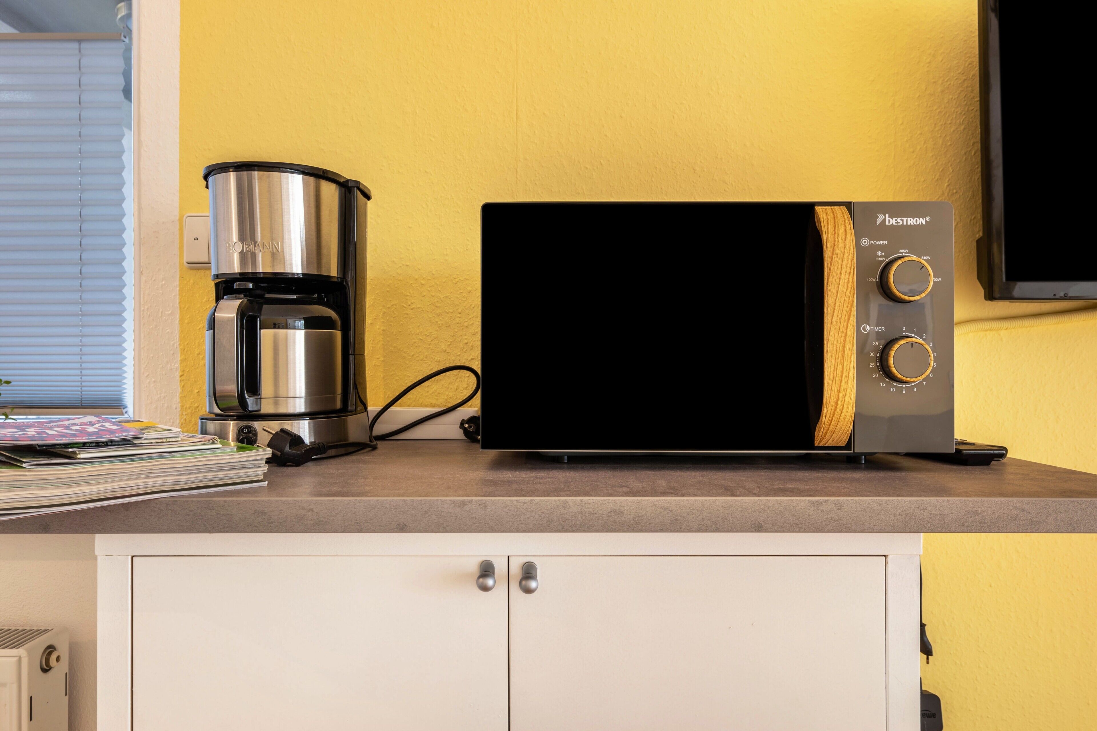 Una kitchenette con cafetera, microondas y televisor sobre una encimera.