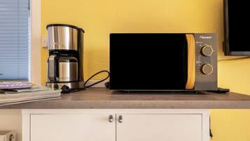 Una kitchenette con cafetera, microondas y televisor sobre una encimera.