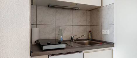 A compact kitchen with a built-in dishwasher, a sink, and a countertop with a bottle and a glass.