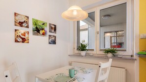 A dining area with a table set for two, a window with potted plants, and wall art.