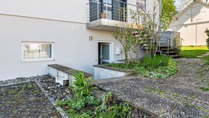 A modern building with a balcony, a door, and a small garden area with plants and gravel.