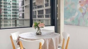 Une table ronde agrémentée d’un arrangement floral, des chaises blanches et une vue sur un bâtiment par la fenêtre.