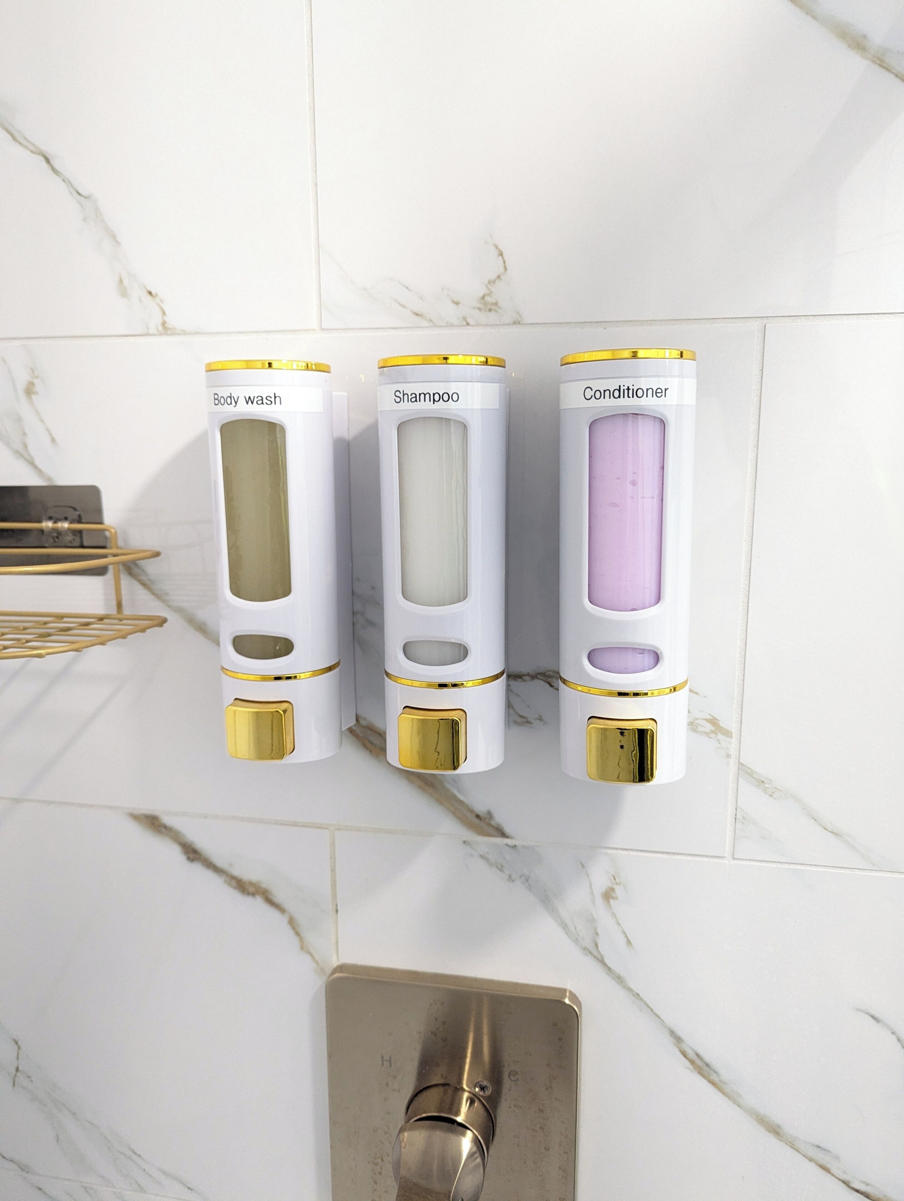 A bathroom with three dispensers labeled body wash, shampoo, and conditioner mounted on a white marble wall.