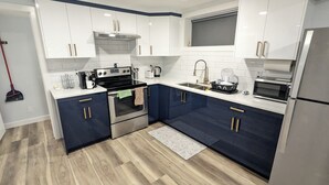 A modern kitchen with white and navy blue cabinets, stainless steel appliances, and a wooden floor.