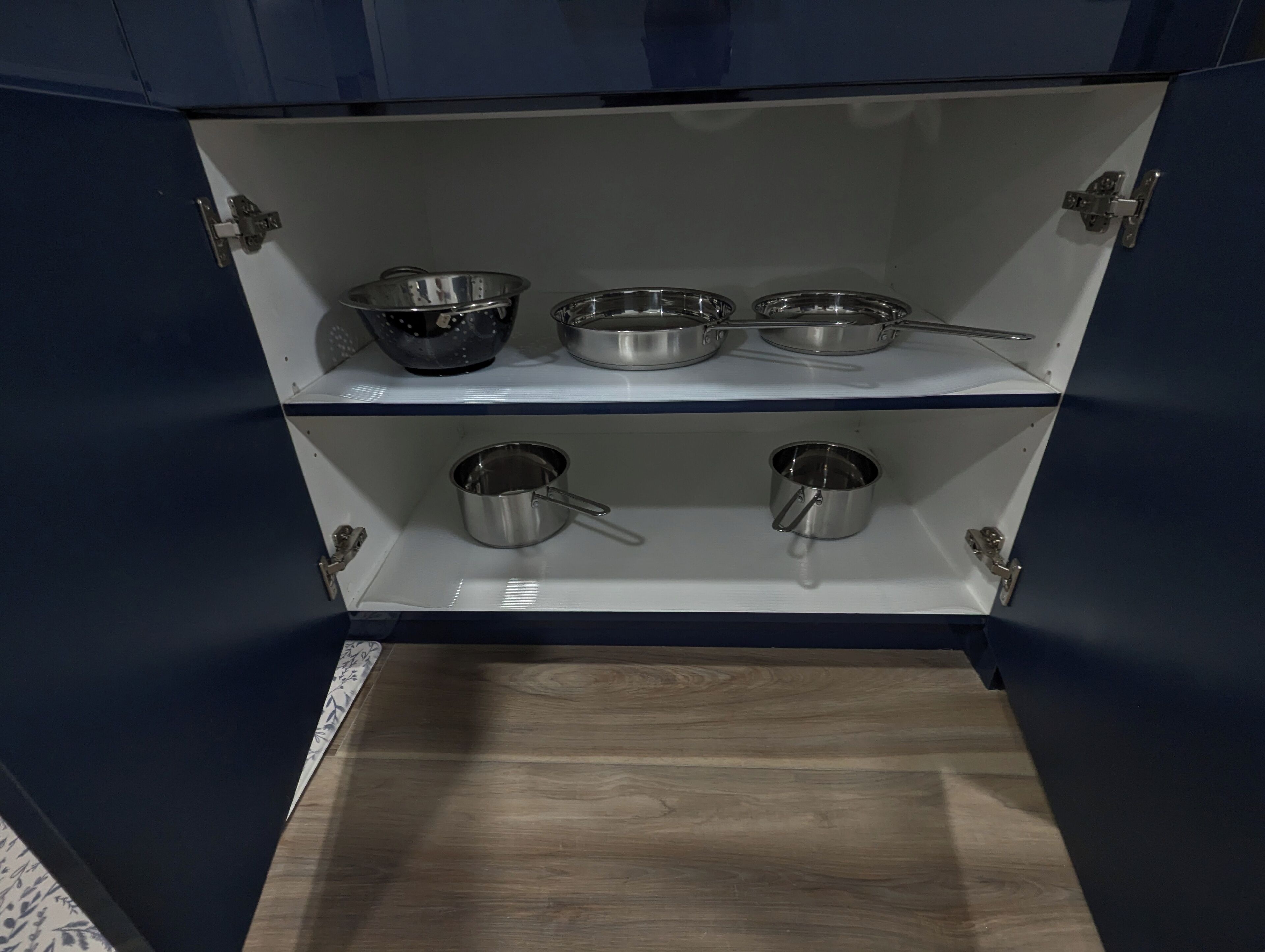 A kitchen cabinet with stainless steel cookware on two shelves.