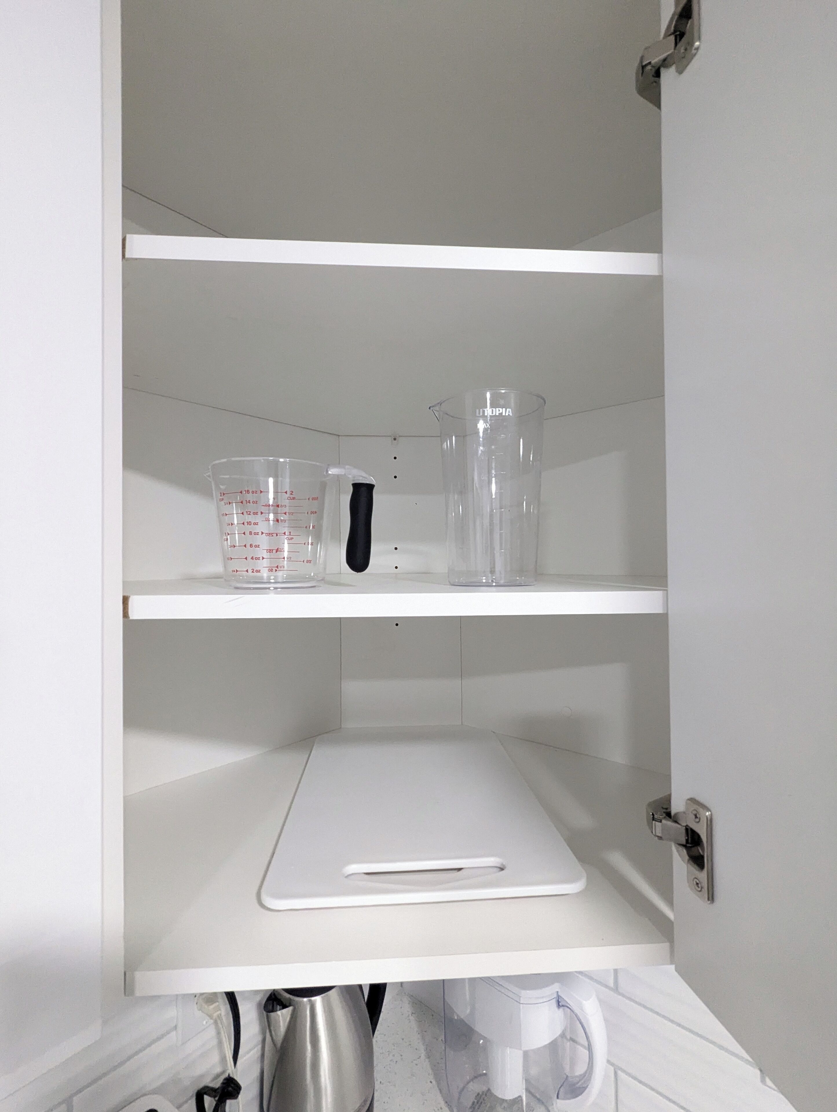 Un meuble de cuisine blanc contenant des tasses à mesurer et une planche à découper.