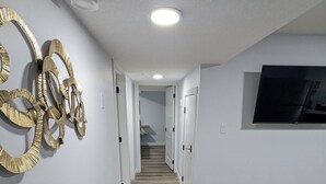 A modern hallway with a wooden floor, a round table with a white marble top, and a large TV on the right wall.