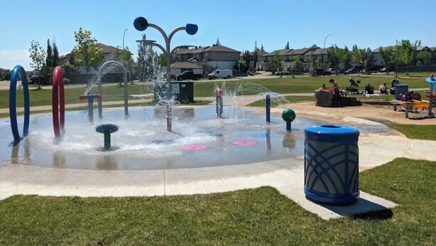 A public park with a water play area, including multiple water jets and colorful rings.