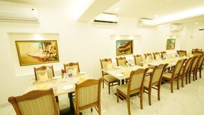 A dining area with long tables and chairs, air conditioning units, and framed artwork on the walls. - YAM HOTEL  (Thiruvananthapuram)