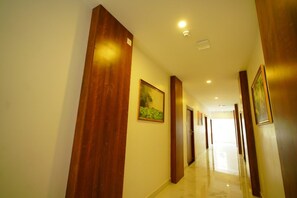 A corridor with wooden doors, a framed picture on the wall, and a light fixture on the ceiling. - YAM HOTEL  (Thiruvananthapuram)