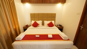 A neatly made bed with a red and white bedspread, two pillows, and two folded towels on the side. - YAM HOTEL  (Thiruvananthapuram)