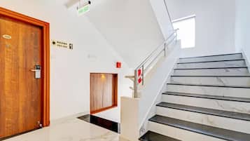 A hotel lobby with a marble floor, a wooden door, a staircase with a handrail, and a fire exit sign.