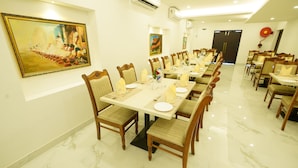 A dining area with long tables, chairs, and artwork on the walls. - YAM HOTEL  (Thiruvananthapuram)