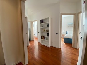 Une pièce spacieuse avec un plancher en bois, une bibliothèque blanche, un lit avec une literie bleue et un mur blanc agrémenté d’une étagère.