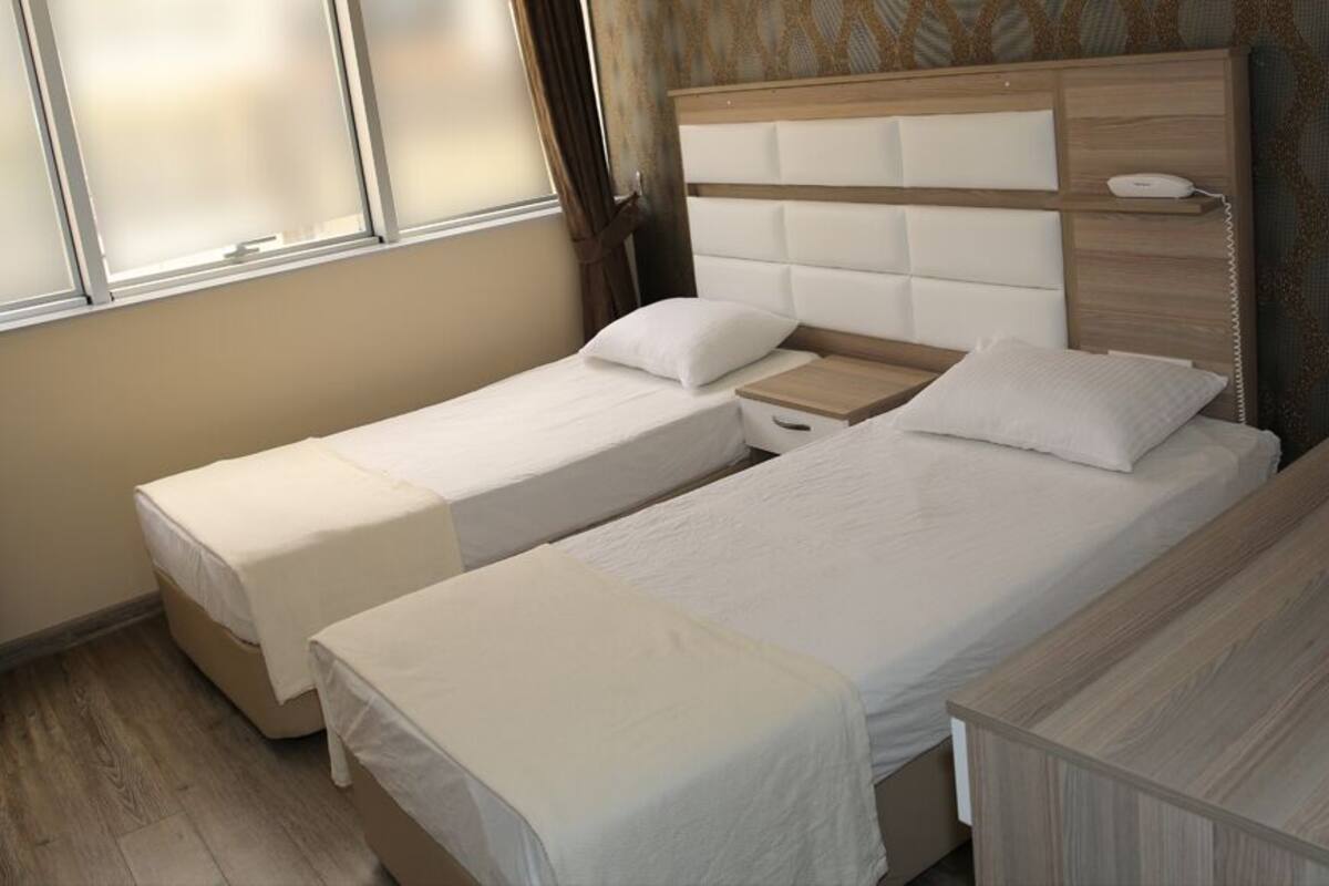 Une chambre d’hôtel avec deux lits simples, une tête de lit en bois, une table de chevet et une petite table de chevet avec une lampe.