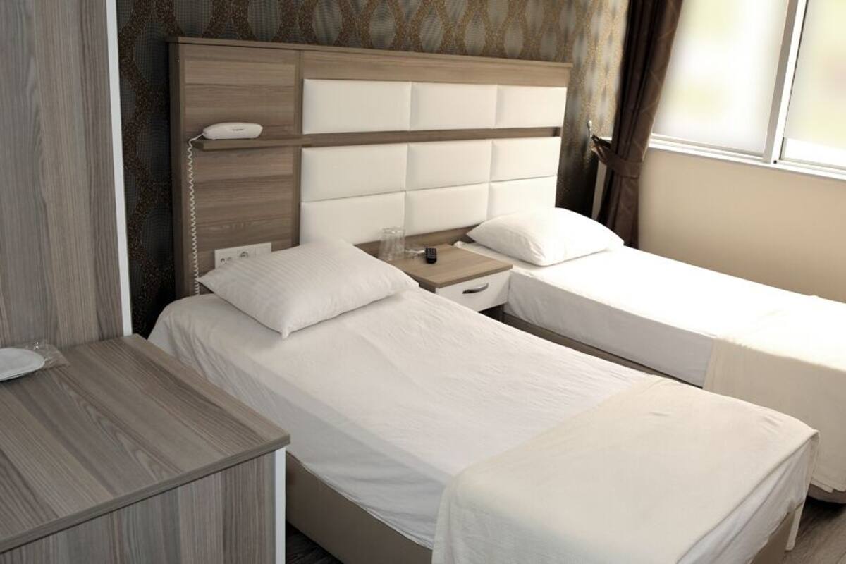 Une chambre d’hôtel avec deux lits simples, une table de chevet en bois et une grande fenêtre.
