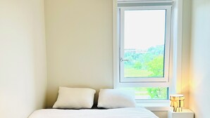 Une chambre à coucher avec un lit, des oreillers, une fenêtre et une lampe de chevet.