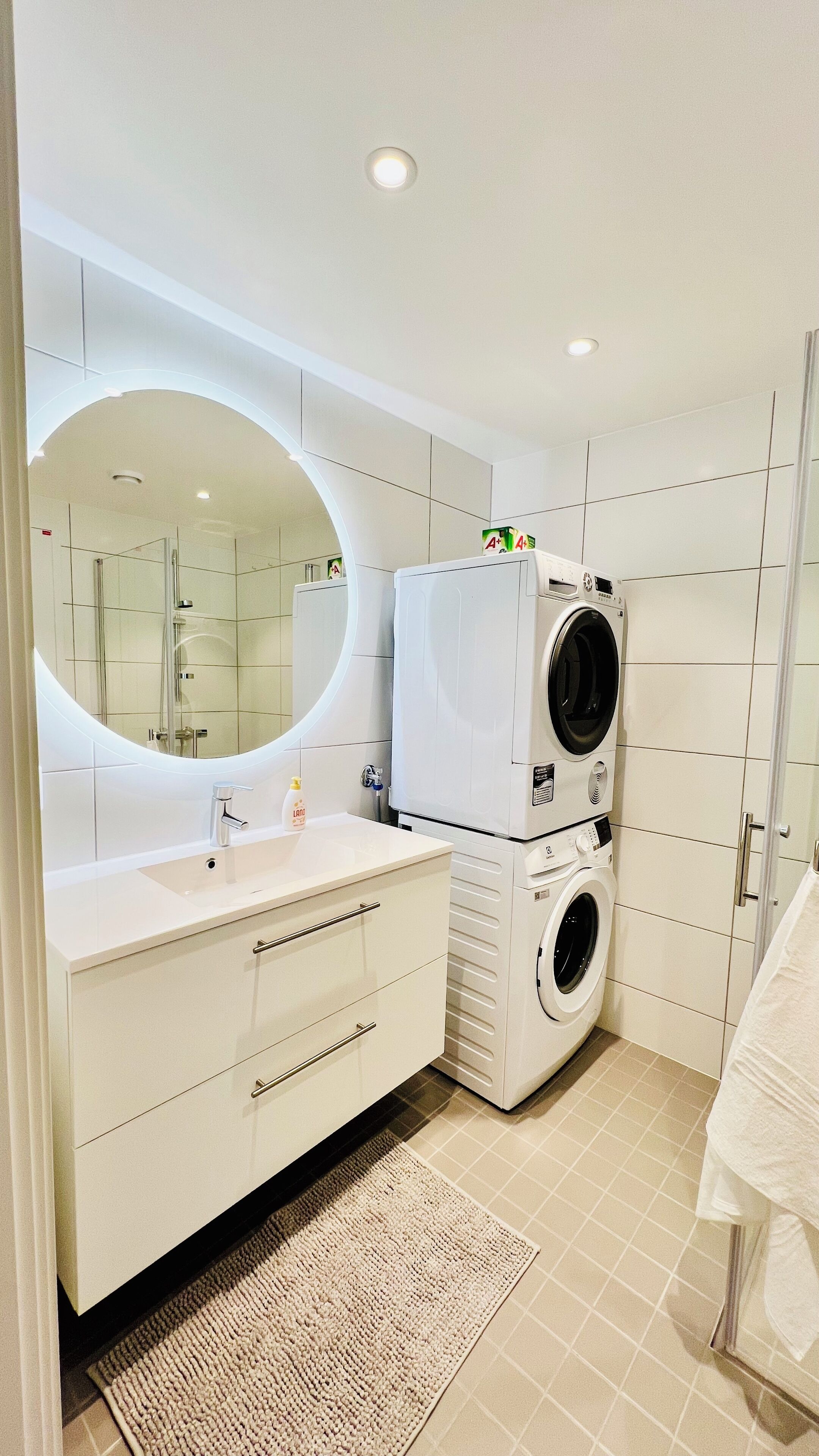 A modern bathroom with a white vanity, a large mirror, a washing machine, and a shower area.