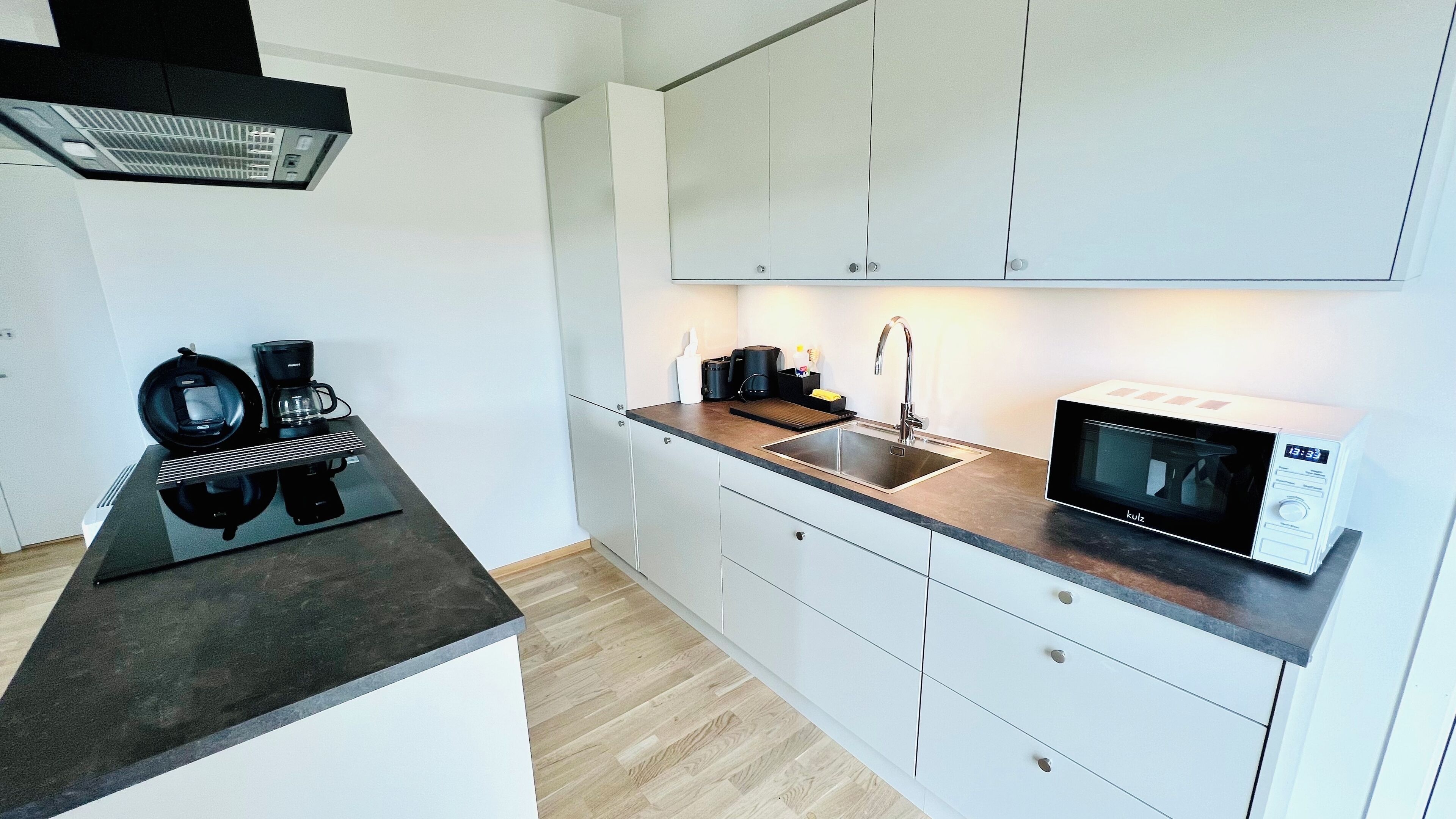 Een moderne keuken met een zwart aanrecht, witte kastjes, een magnetron, een koffiezetapparaat en een spoelbak.