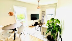 Un salon moderne doté d’un téléviseur à écran plat, d’une table à manger avec des chaises, d’une table basse et d’une grande plante en pot.