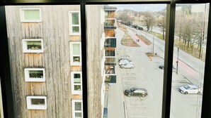 Une vue depuis un immeuble de grande hauteur, avec de nombreuses fenêtres, un ciel dégagé et une rue où sont garées des voitures et où l’on peut voir des piétons.