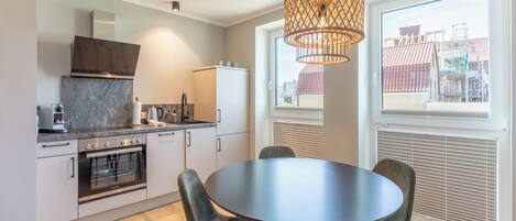 A modern kitchen with a round dining table and chairs, a built-in oven, and a large window with blinds.