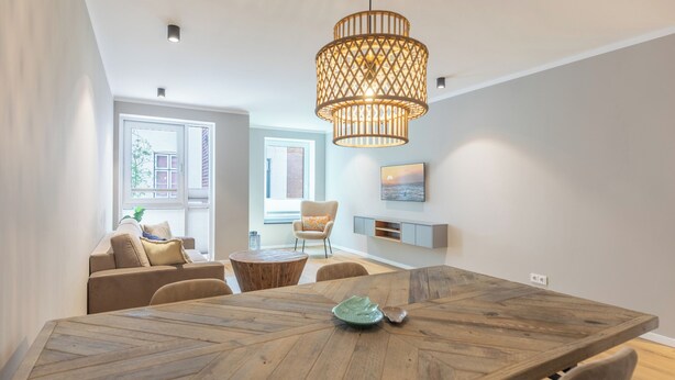 A modern dining area with a wooden table, chairs, and a hanging light fixture. - Deluxe apartment Zollbude 02 directly at Husum harbor (Husum)
