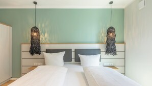 A modern bedroom with two beds, a wooden headboard, and hanging pendant lights. - Apartment Zollkoje 03 directly at the Husum harbor (Husum)