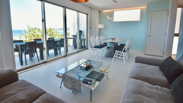 A modern living room with a glass dining table, a sofa, and a balcony with outdoor seating. - Ocean View Ishigaki Kaze & Nami (Ishigaki)