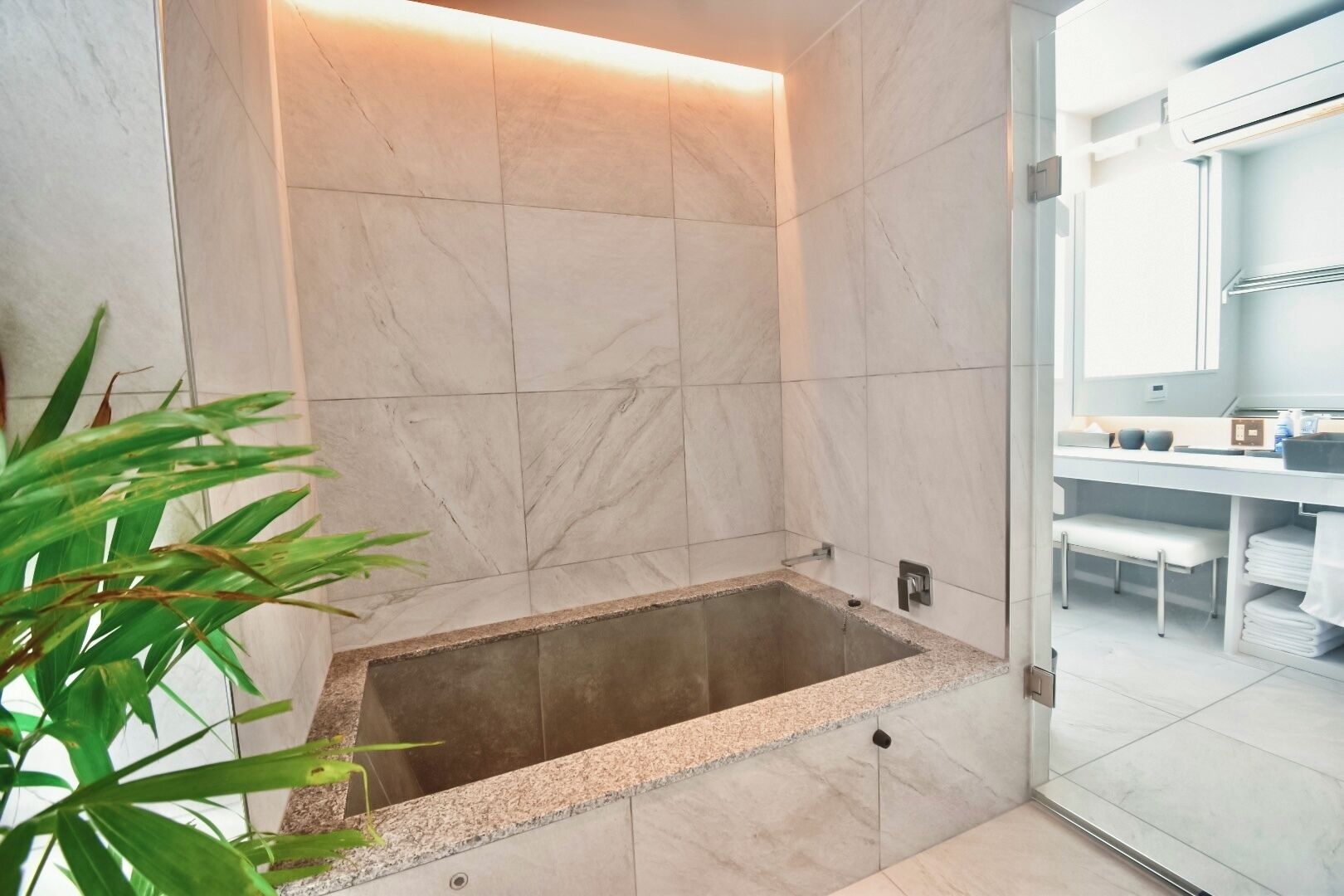 Een moderne badkamer met een vrijstaand bad, marmeren wanden en een zichtbaar wastafelgedeelte met handdoeken.