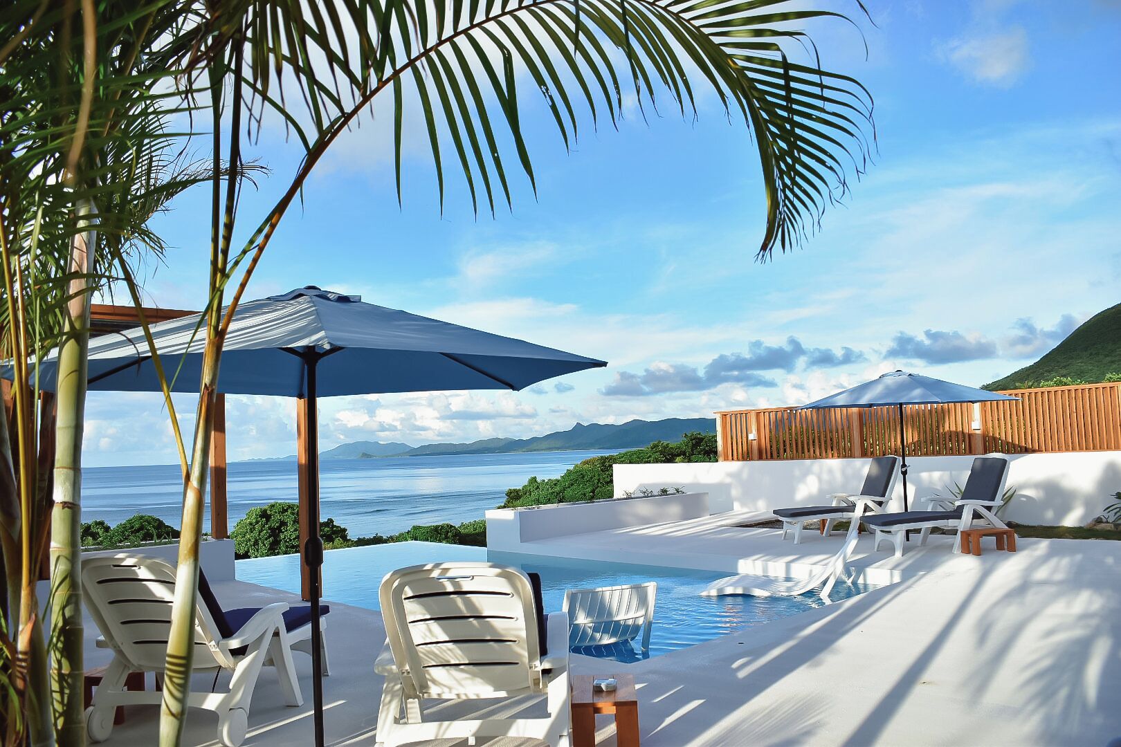 A poolside area with lounge chairs, umbrellas, and a view of the sea.