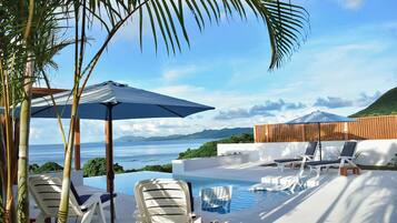 A poolside area with lounge chairs, umbrellas, and a view of the sea.