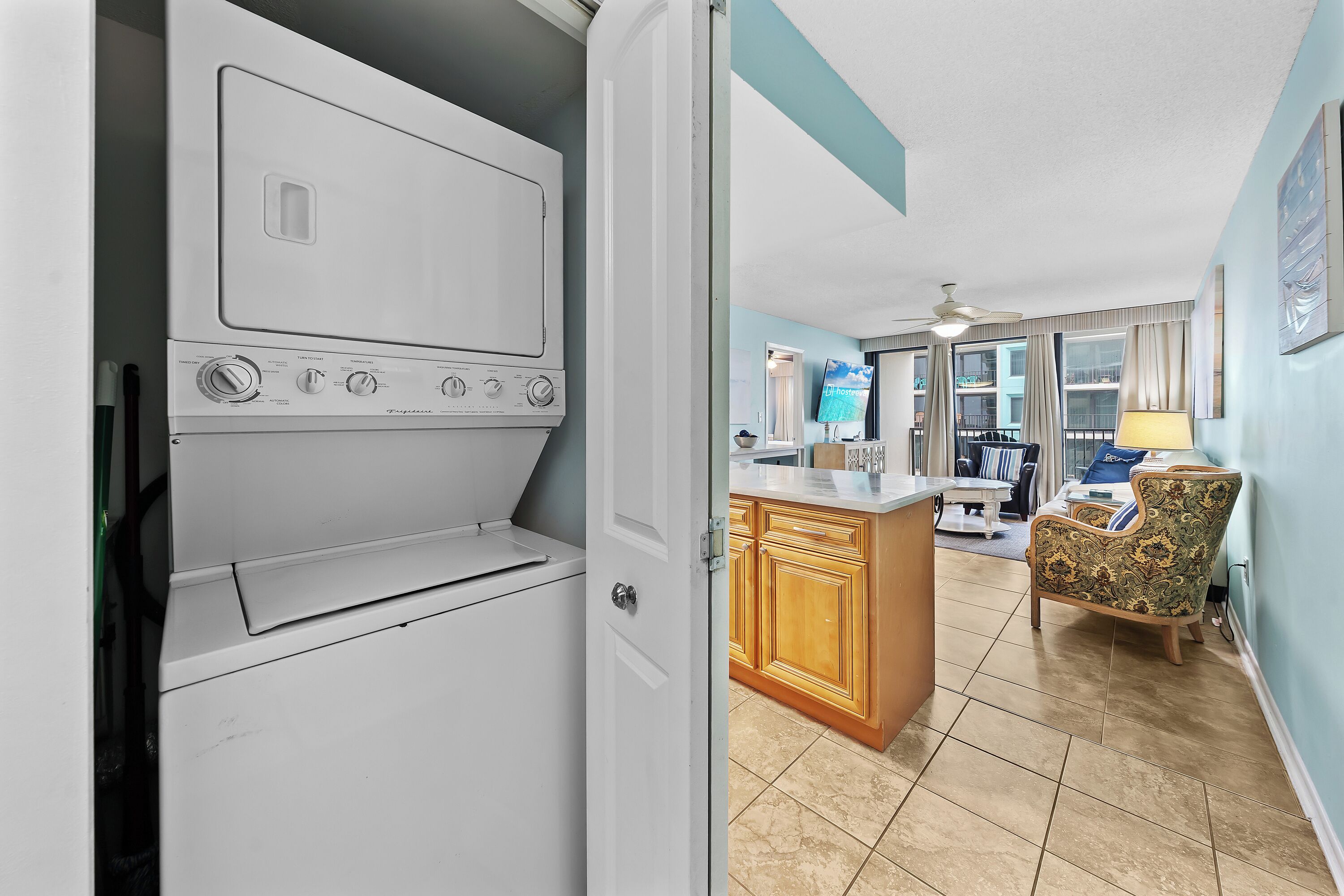 A laundry room with a white washer and dryer, wooden cabinets, a patterned chair, and a kitchen area with a counter and cabinets.