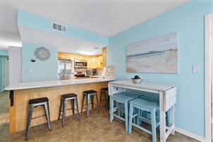 A modern kitchen with a white island, bar stools, and a blue accent wall.