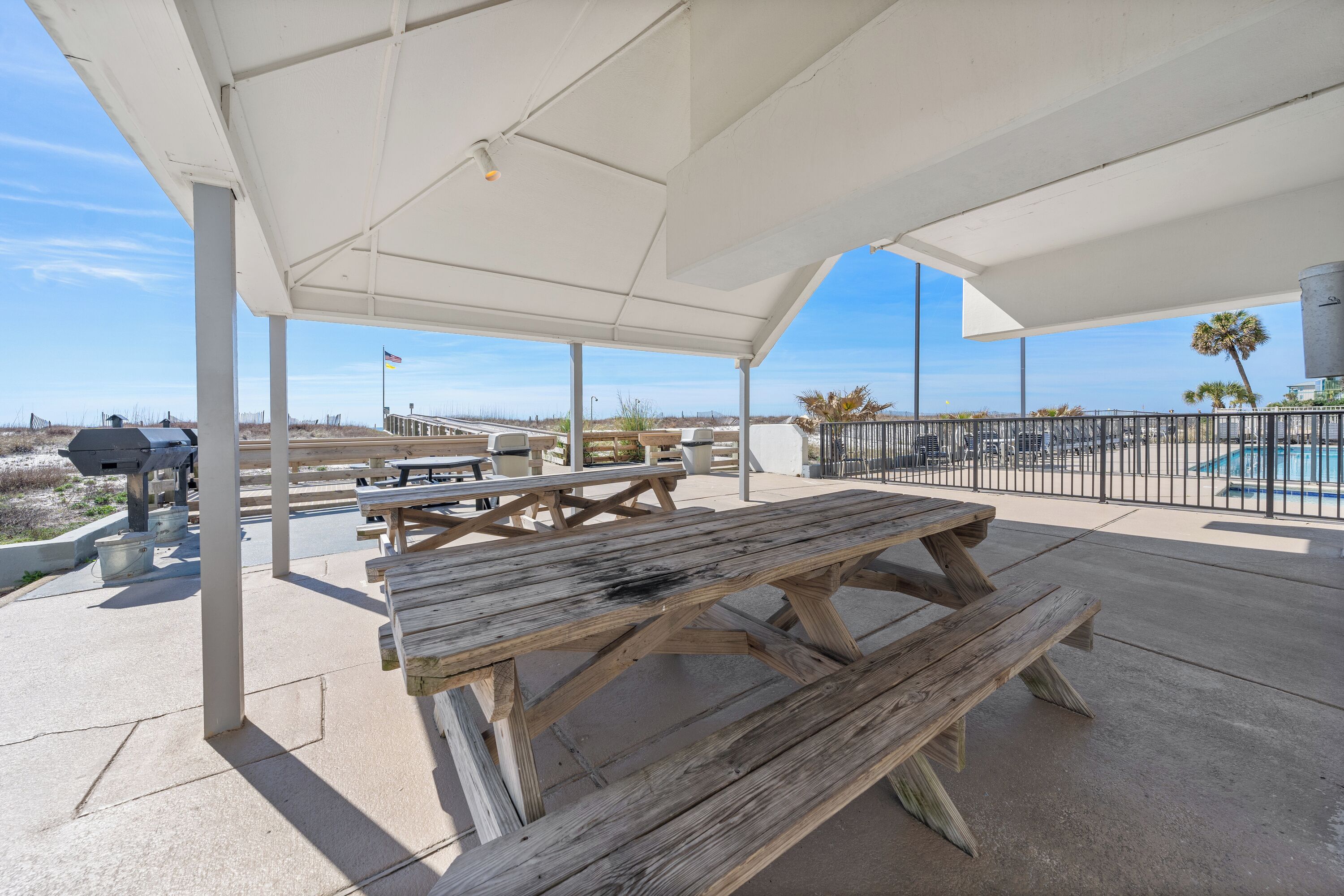 Une terrasse extérieure avec des tables de pique-nique et un barbecue, le tout installé sous un auvent blanc.