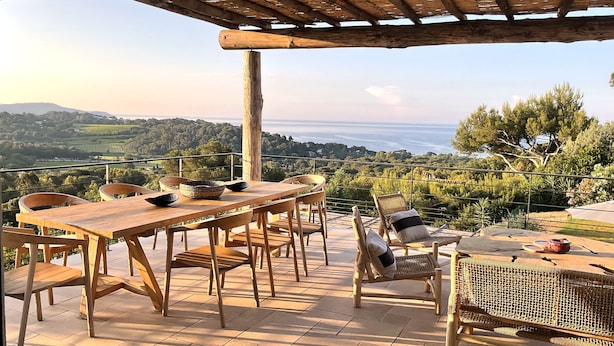 Un patio al aire libre con una mesa y sillas de madera, un banco de mimbre y vistas al campo.