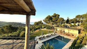 Zona de piscina con sillones de descanso y una pérgola de madera, rodeada de abundante vegetación y vistas al mar.
