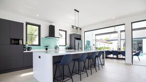Une cuisine moderne dotée d’un îlot central, de tabourets de bar et offrant une vue sur l’espace piscine extérieur.