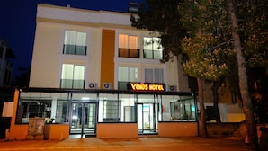 Un hotel con un letrero que dice 'Venus Hotel' en la entrada, amplias ventanas y un árbol en primer plano.