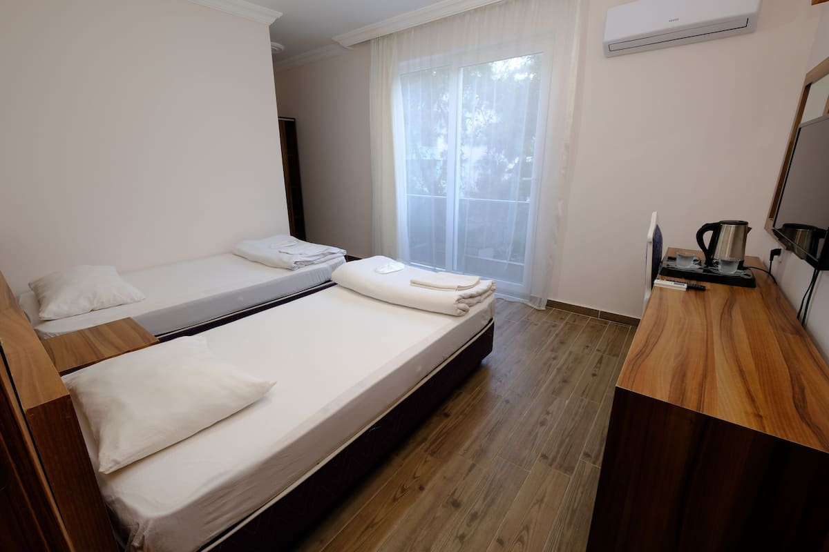 Una camera d'albergo con due letti, una scrivania in legno, una macchina per il caffè e una finestra con tende leggere.