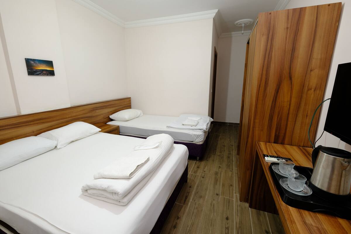 Una camera d'albergo con due letti, una testiera in legno, un piccolo quadro appeso al muro e una scrivania con bollitore e tazze.