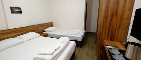 A hotel room with two beds, a wooden headboard, a small painting on the wall, and a desk with a kettle and cups.