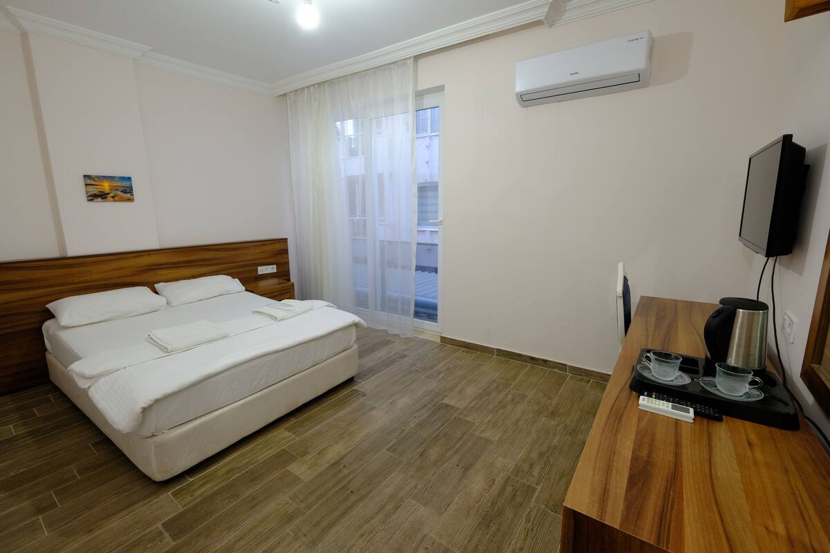 Una camera d'albergo con un letto, una scrivania in legno con un bollitore, una televisione e un condizionatore d'aria.