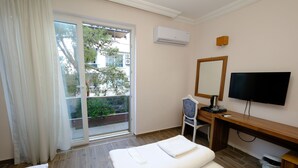 Habitación de hotel con cama, escritorio con computadora, televisor y puerta corrediza al exterior.