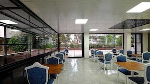 Un área de estar interior amplia, con mesas y sillas, ventanas grandes y vistas al exterior.