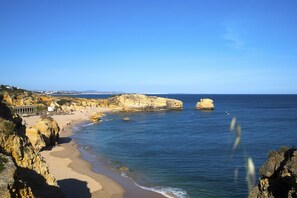 A coastal beach with rocky cliffs, a sandy shore, and a clear blue sky.