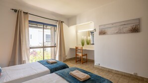 Een slaapkamer met twee bedden, een bureau, een stoel en een raam met gordijnen.